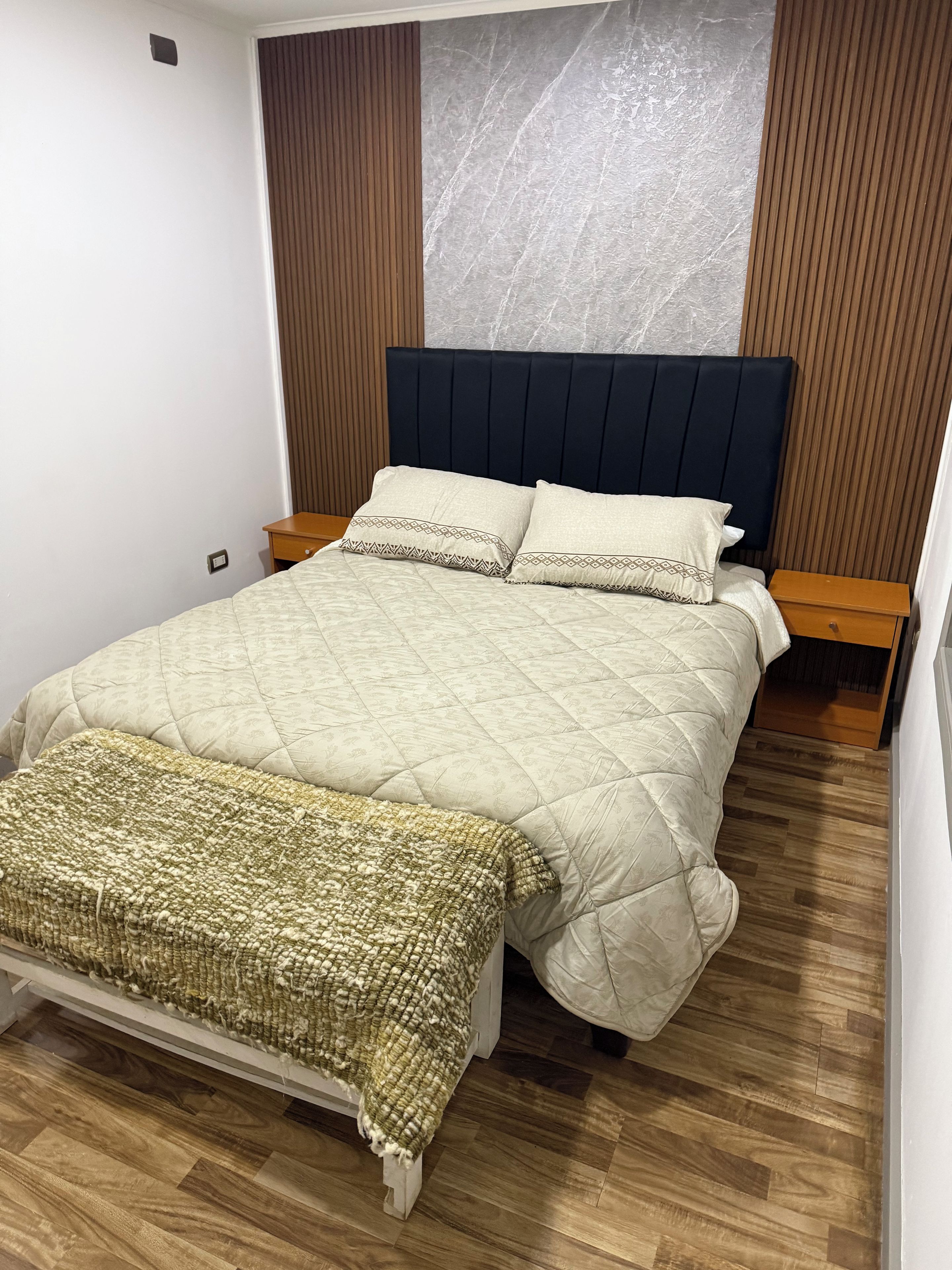 Un lit bien fait, avec une tête de lit matelassée, une table de chevet et un plancher en bois.