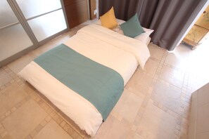 A bed with a white and green bedspread, a yellow pillow, and a green pillow. - Spacious Private Stay Near Higashi-Shinjuku | Sleeps 10 | Families & Groups | WiFi (2) (新宿区新宿７丁目)