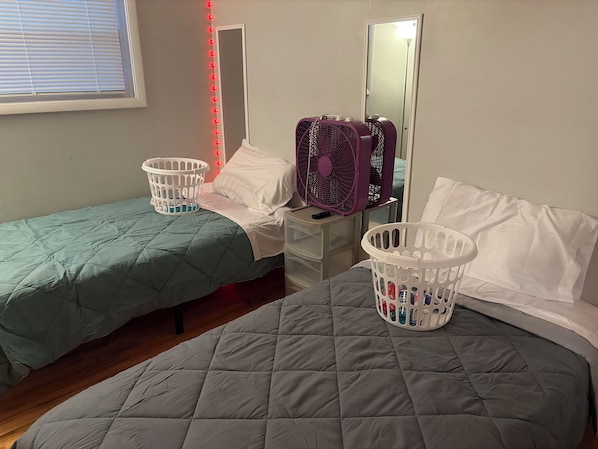 A bedroom with two beds, a nightstand, a mirror, and two laundry baskets.