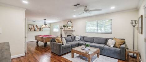 A living room with a pool table, a gray sectional sofa, a coffee table, and a fireplace.