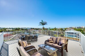 A deck with outdoor furniture, a glass table, and a view of a swimming pool and buildings. - Waterfront Marco Retreat: Pool, Dock, Game Room + Beach Gear (Marco Island)