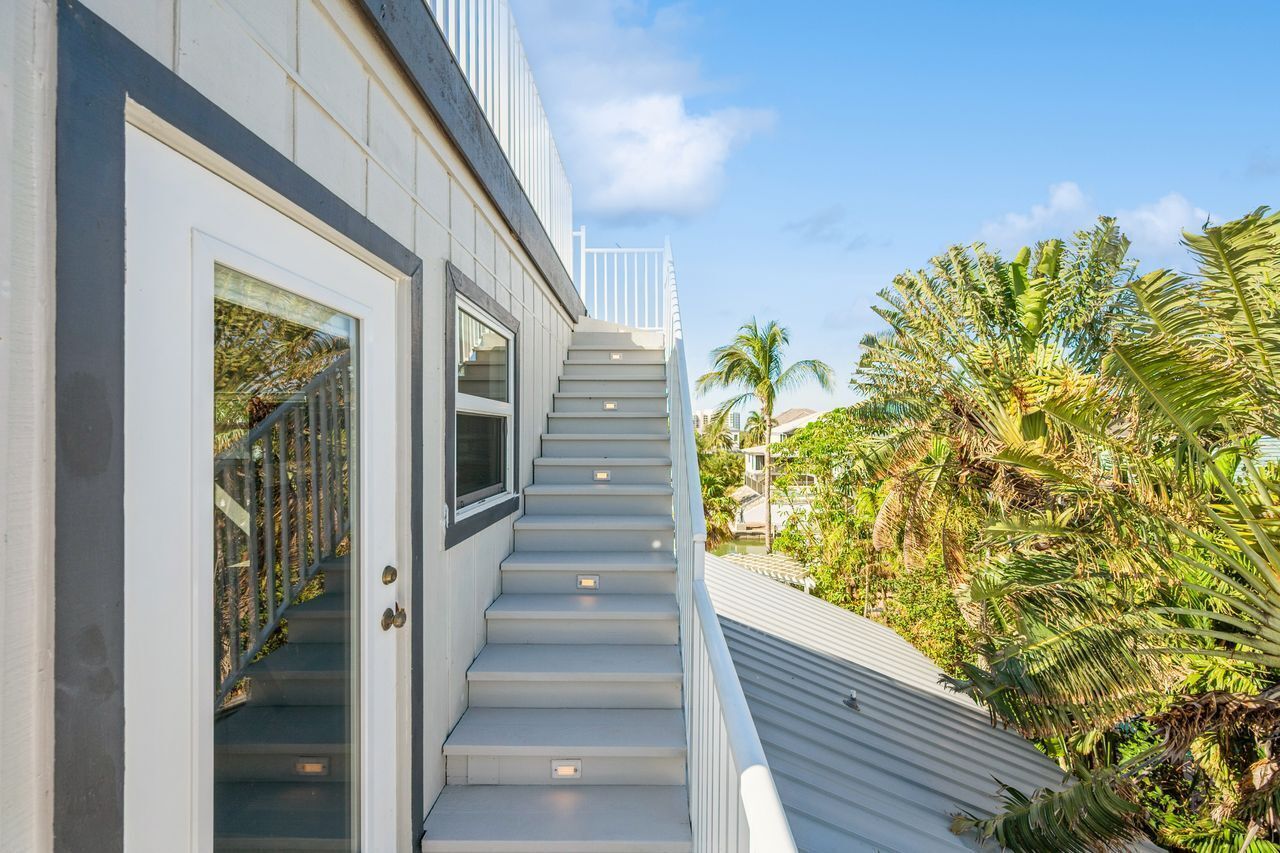 A modern building with a staircase leading to a balcony, surrounded by lush greenery.
