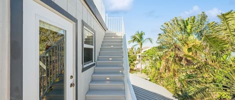 A modern building with a staircase leading to a balcony, surrounded by lush greenery.