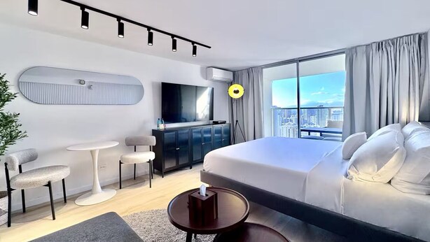 Quarto de hotel moderno com uma cama grande, escrivaninha, cadeira, televisão e vista para a cidade.