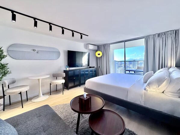Ein modernes Hotelzimmer mit einem großen Bett, einem Schreibtisch, einem Sessel, einem Fernseher und Blick auf die Stadt.