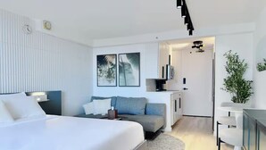 Quarto de hotel moderno com uma cama grande, um sofá, uma escrivaninha e uma televisão.
