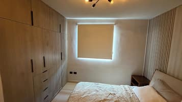Et soveværelse med en seng, et skab, et vindue og en lampe i loftet.