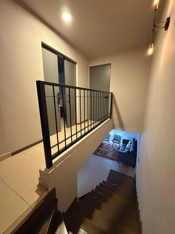 Un escalier avec une rampe noire menant à un palier où se trouvent un canapé et une petite table.
