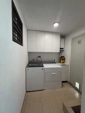 Une petite buanderie équipée d’un lave-linge, d’un sèche-linge et d’un chauffe-eau.