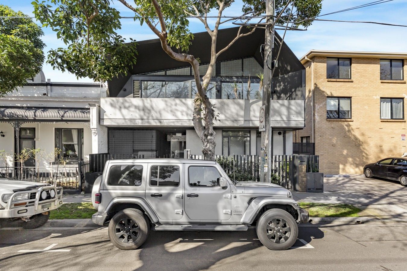 A modern two-story building with a garage, a tree in front, and a parked white SUV.