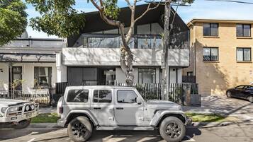 A modern two-story building with a garage, a tree in front, and a parked white SUV.