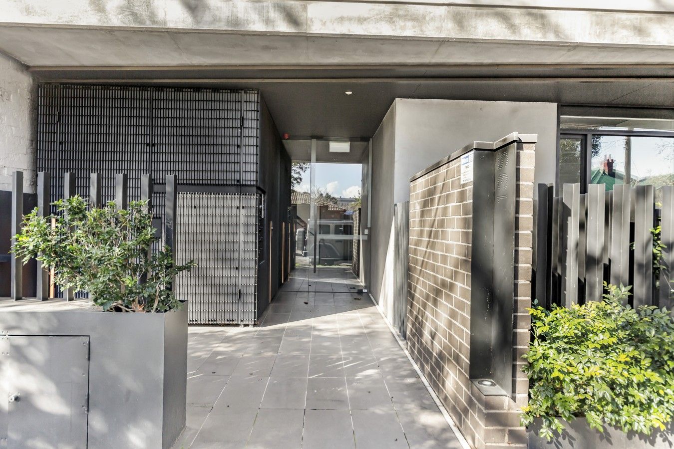 A modern building with a covered walkway, metal gates, and a brick wall.