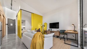 Ein modernes Wohnzimmer mit einer Couch, einem Schreibtisch, einem Sessel, einem Fernseher und einer Glastrennwand.