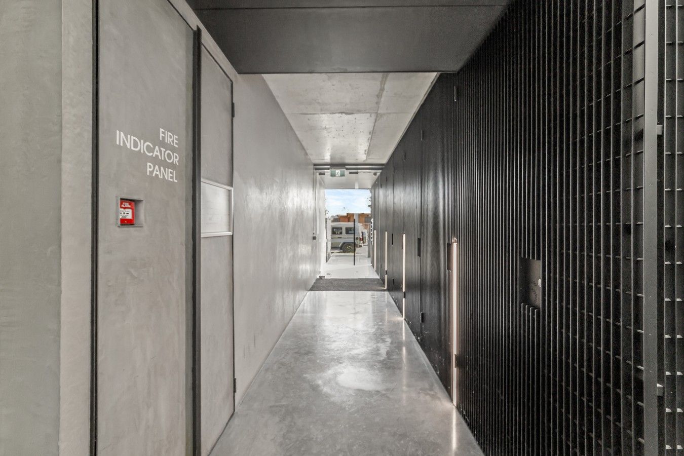 A corridor with a fire indicator panel on the left and a metal security gate on the right.