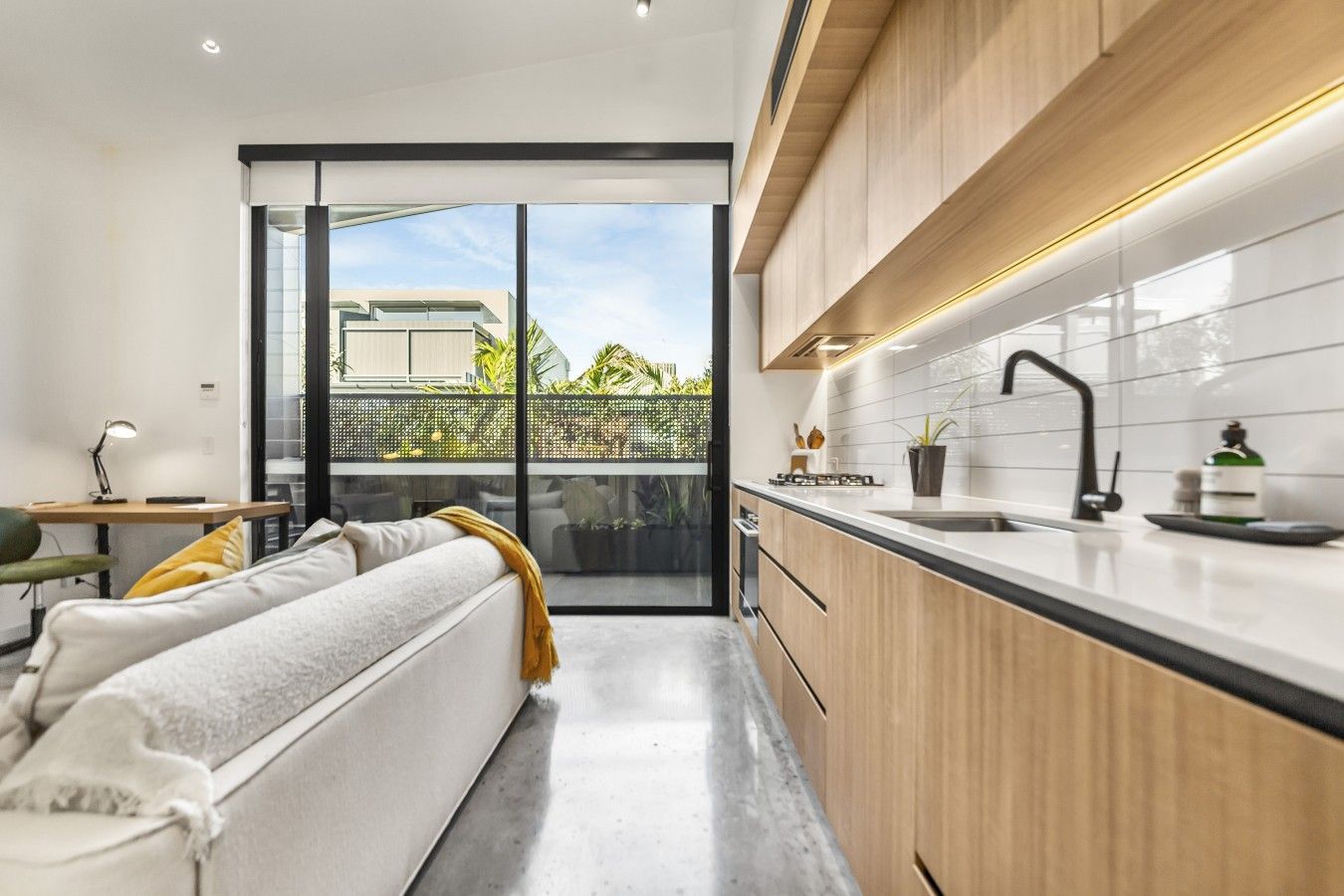Eine moderne Küche mit einer Schiebetür zum Balkon, einer Couch mit Kissen sowie einem Essbereich mit Tisch und Stühlen.