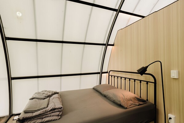 Un lit simple avec une tête de lit, une lampe de chevet et une prise de courant au mur.