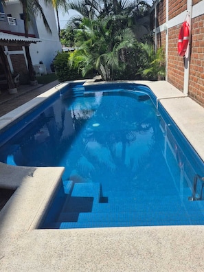 A swimming pool with clear blue water, surrounded by a brick wall and palm trees. - Your ideal winter retreat in the Villa Obregón neighbourhood  Melaque! (San Patricio)