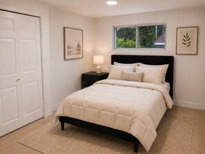 Un dormitorio con cama, mesita de noche, lámpara, ventana y dos cuadros en la pared.