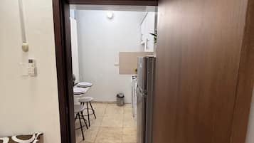 A narrow hallway leading to a kitchen with a refrigerator and a dining area.