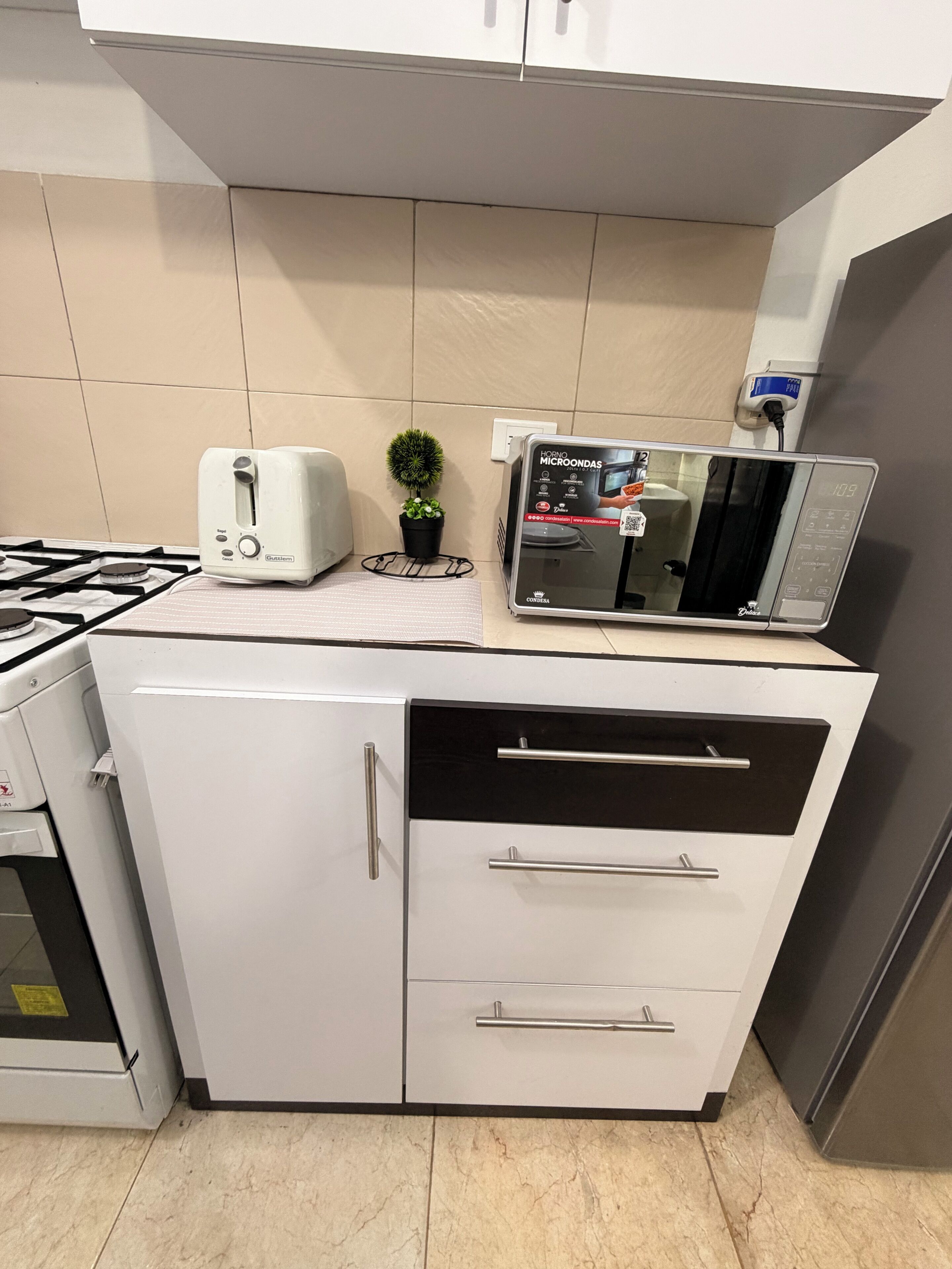 A kitchen with a gas stove, a toaster, a microwave, and a small potted plant.