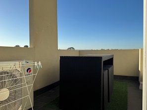 A rooftop terrace with a large air conditioning unit, a black outdoor seating area, and a clear view of the sky.