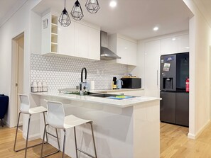 A modern kitchen with a central island, white cabinetry, a microwave, a refrigerator, and a hexagonal tile backsplash.