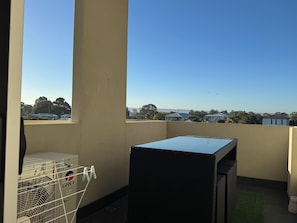 A balcony with a view of houses and trees, a black grill, and a white laundry basket. - Blissful Modern Apartment (Cloverdale)
