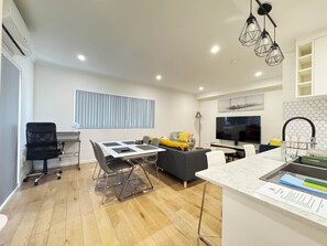 Een moderne woonkamer met een eethoek, een keuken met een marmeren aanrecht en een grote flatscreen-televisie.