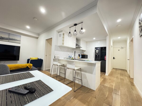 A modern kitchen with a central island, bar stools, and a dining area with a TV and remote controls.