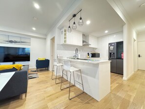 A modern kitchen with a central island, white cabinetry, and a stainless steel refrigerator. - Blissful Modern Apartment (Cloverdale)