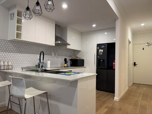 A modern kitchen with white cabinetry, a central island, and a black refrigerator. - Blissful Modern Apartment (Cloverdale)