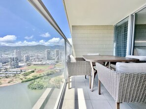 Ein Balkon mit Tisch und Korbstühlen, mit Blick auf eine Stadtlandschaft und einen Fluss.