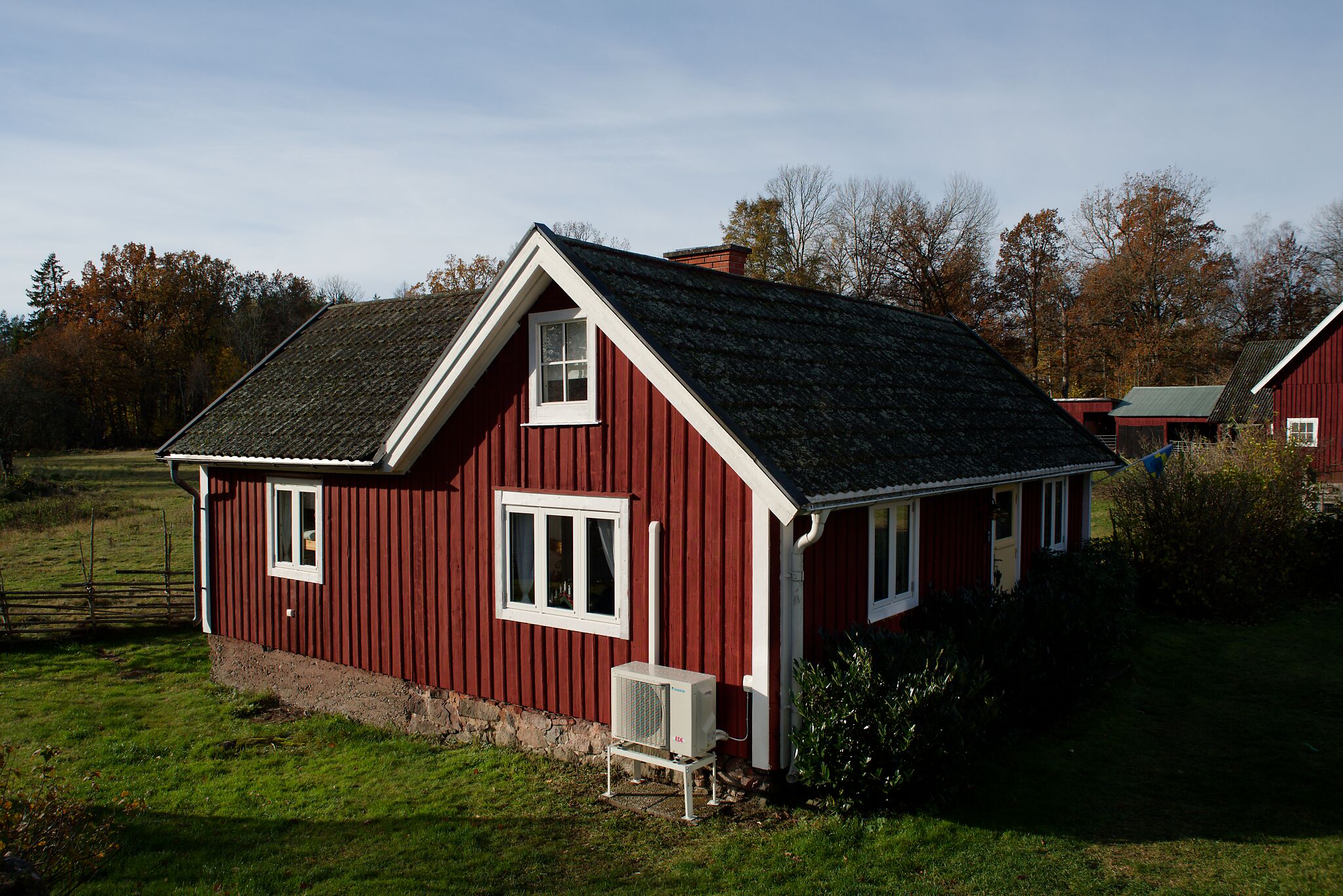 Ett rött trähus med ett sluttande tak, en liten veranda och ett fönster.