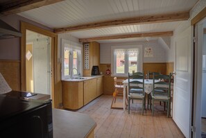 A kitchen with wooden cabinets, a sink, and a dining area with chairs and a table. - Charming Swedish Cottage in Torsås, Småland (Torsås)