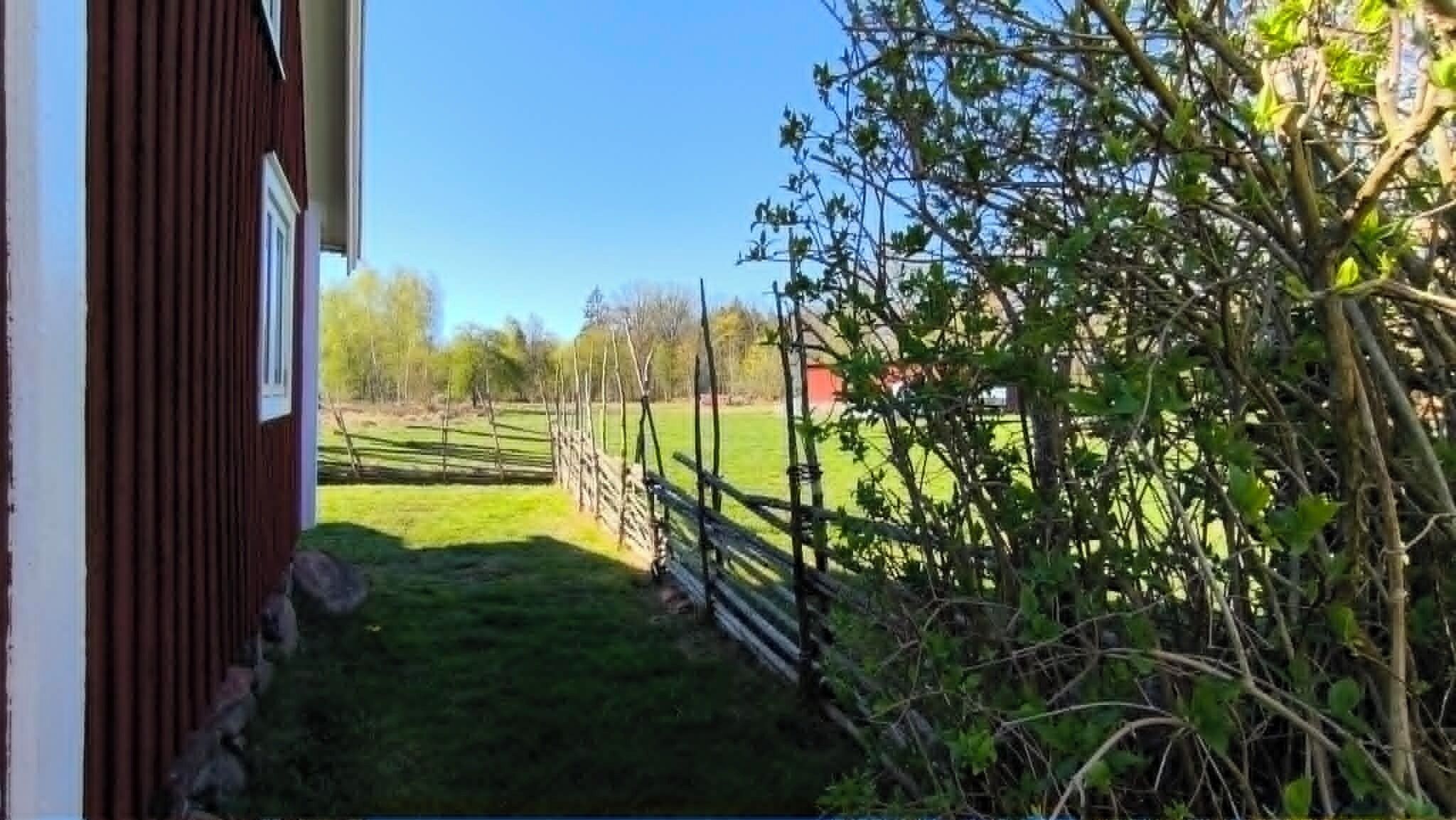 A rural property with a wooden fence, a red building, and a green field.