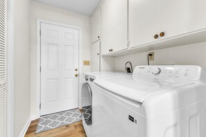 A laundry room with a front-loading washing machine, a door with a doorknob, and a patterned doormat. - Spacious 4-bedroom house with large backyard near Maxwell AFB (Montgomery)