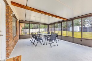 Une terrasse couverte avec une table et des chaises, de grandes fenêtres et un mur en briques.