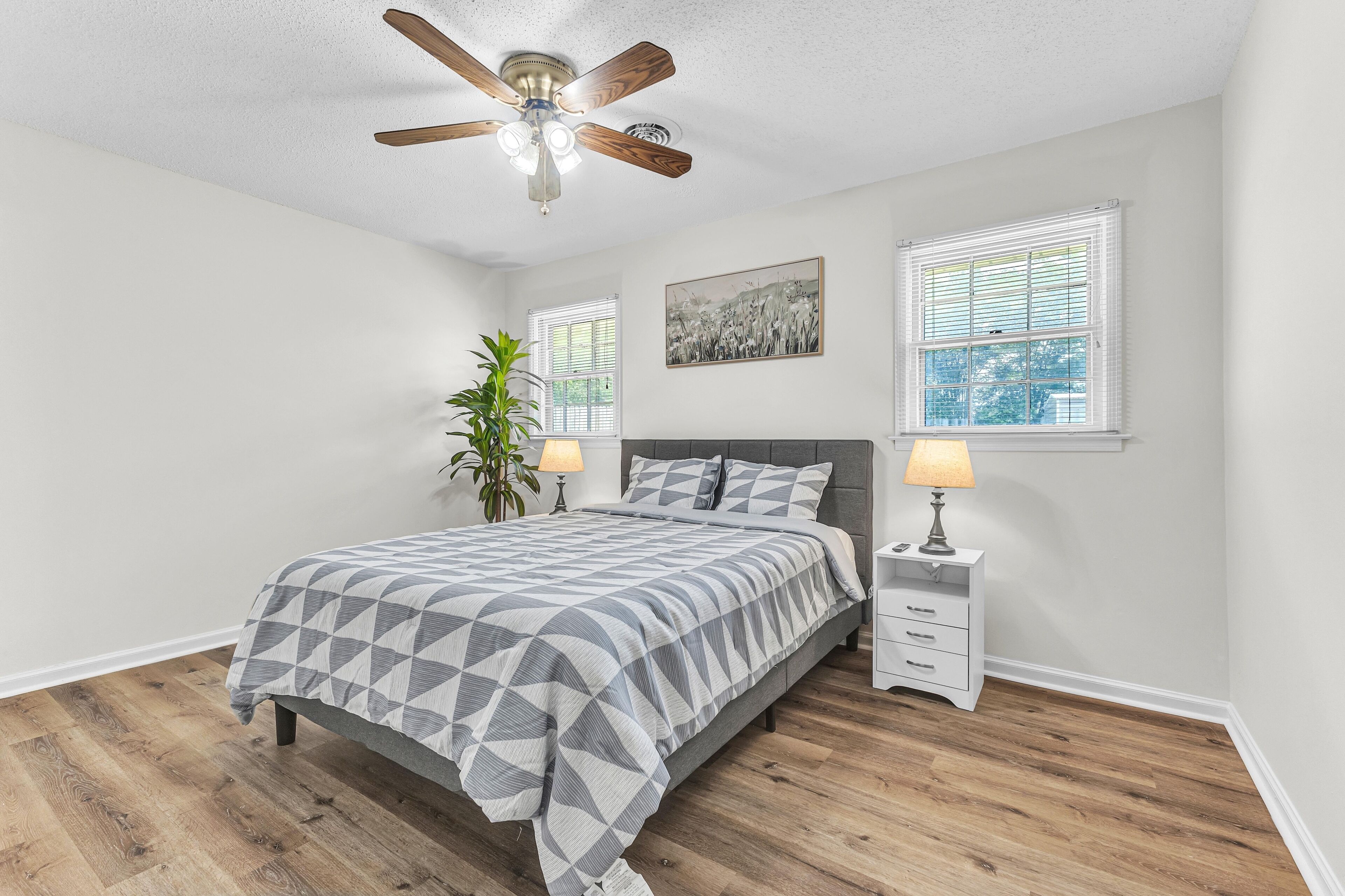 A bedroom with a bed, nightstands, a ceiling fan, and two windows with blinds.