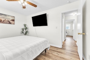 Een slaapkamer met een bed, een tv aan de muur, een plafondventilator, een plant en een schilderij.