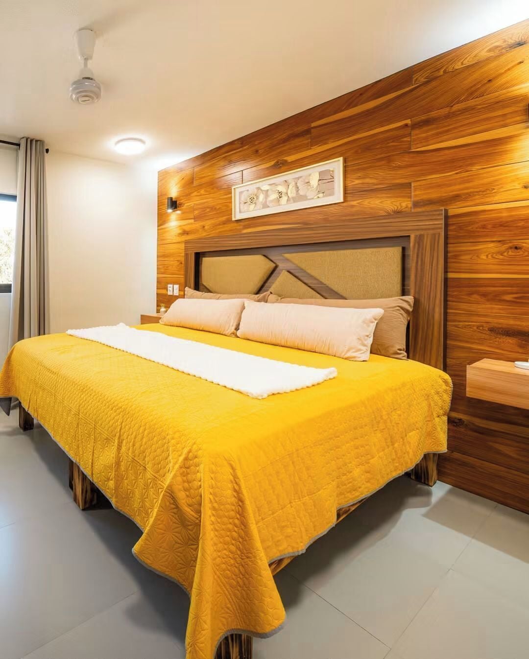 Un lit avec une couette jaune, une tête de lit en bois et un tableau accroché au mur.