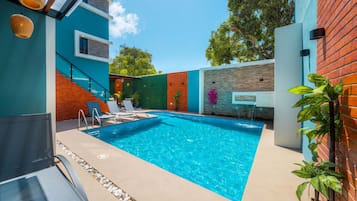 Une piscine extérieure moderne, avec une eau d’un bleu limpide, entourée d’un mur extérieur aux couleurs variées, d’un escalier en bois et d’un espace détente avec des chaises longues.