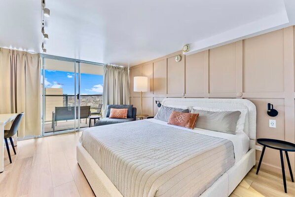 Ein Hotelzimmer mit einem großen Bett, einem Schreibtisch, einem Stuhl, einem Nachttisch und Blick auf die Stadt durch das Fenster.