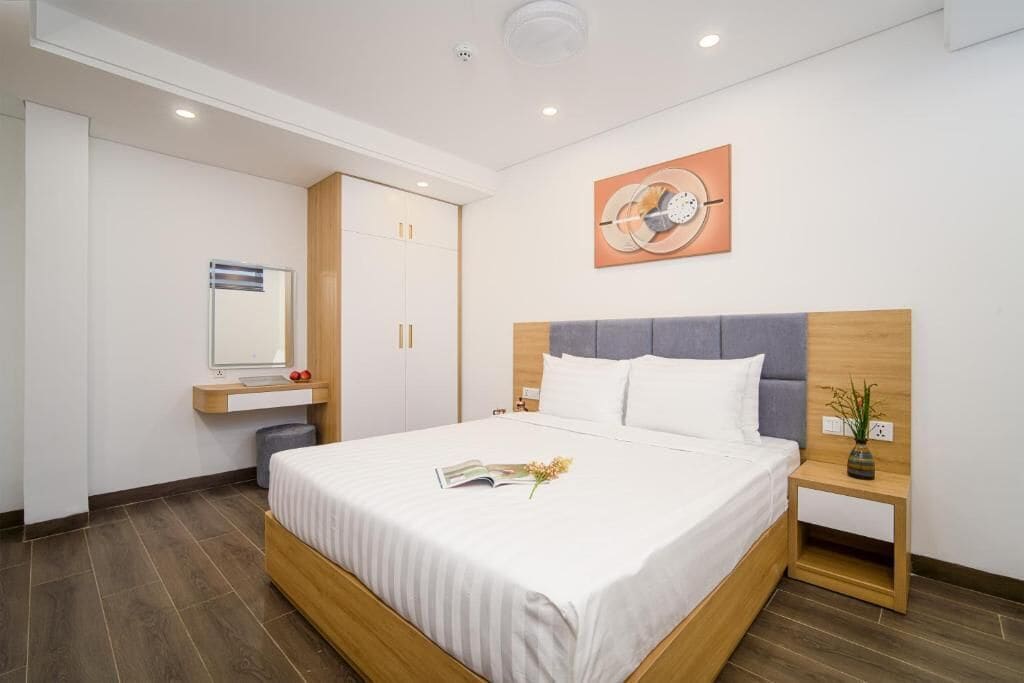 A modern hotel room with a large bed, a bedside table with a vase, and a wall-mounted artwork.