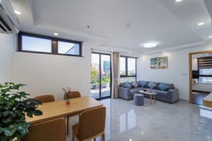 A modern living room with a dining area, a gray sofa, and a large window.