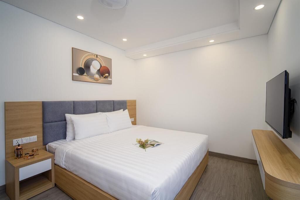 A hotel room with a bed, bedside table, TV, and artwork on the wall.