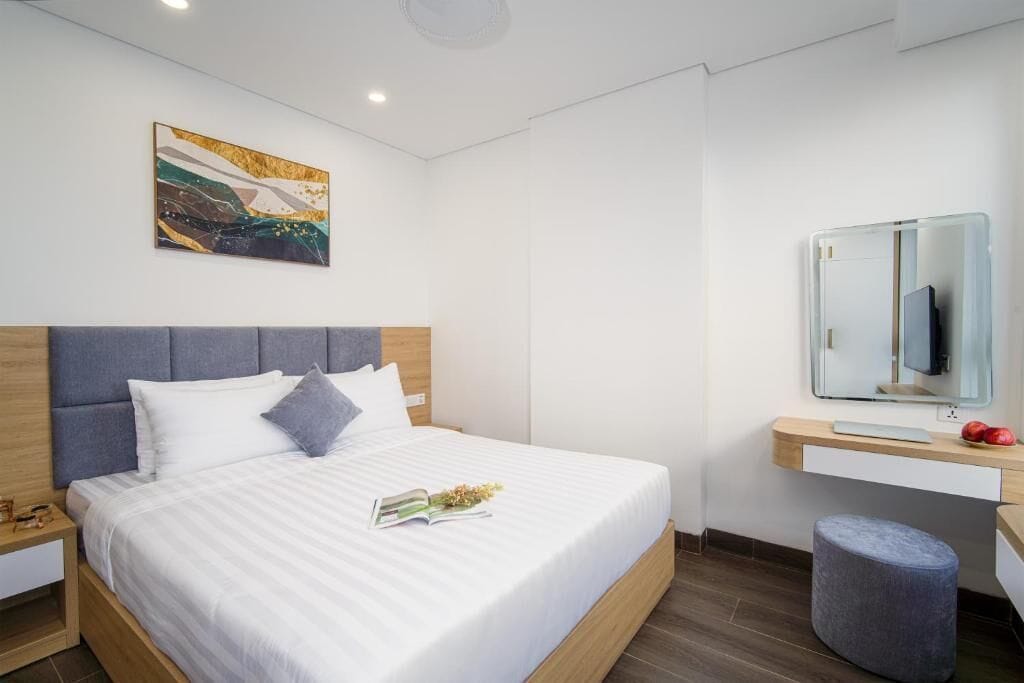 Ein modernes Hotelzimmer mit einem großen Bett, einem Nachttisch, einem Schreibtisch mit Computer, einem Sessel und einem großen Spiegel.