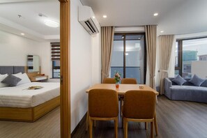 A hotel room with a bed, a dining table with chairs, a sofa, a window with curtains, and an air conditioning unit. - HSuites Riverside Hotel & Apartment  (An Hai)