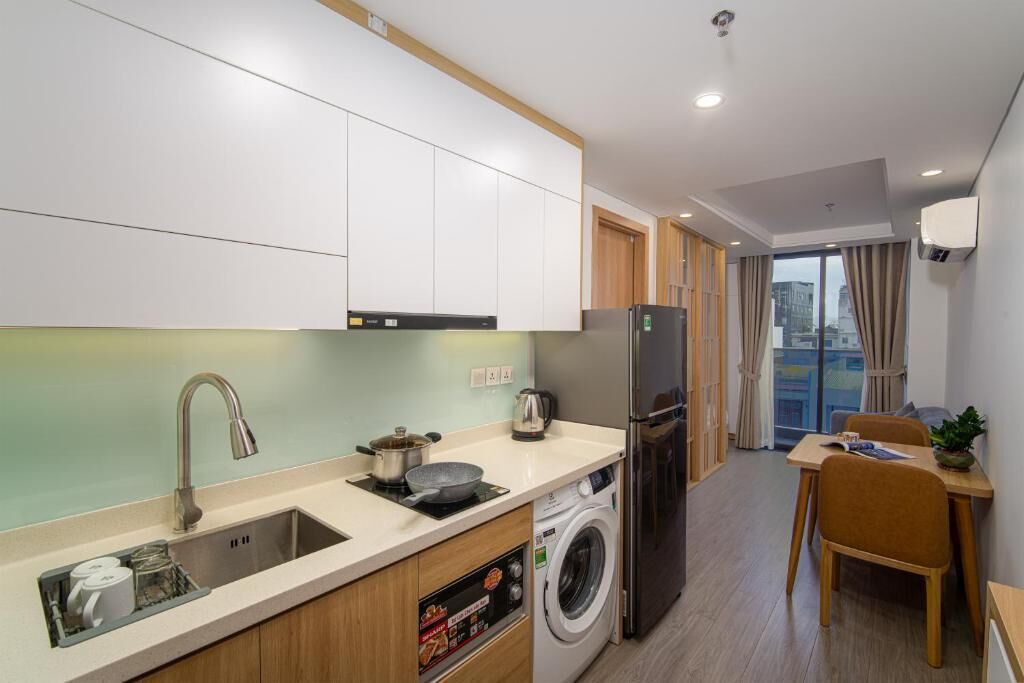 A compact kitchen with a sink, stove, and washing machine, a dining area with a table and chairs, and a view through a large window.
