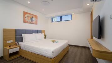 A modern bedroom with a wooden bed frame, a nightstand, a flat-screen TV mounted on the wall, and a window providing natural light.