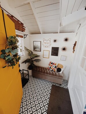 Ein Zimmer mit einem gemusterten Boden, einem braunen Sofa mit Kissen, einer Zimmerpflanze und Wanddekorationen, darunter ein Bären-Form-Objekt und Sternschnuppen-Muster.
